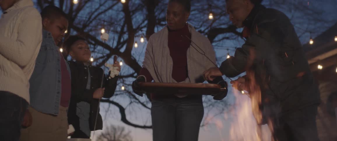 Family roasting marshmallows on fire pit in backyard at night
