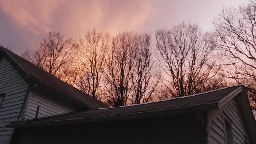 Trees are visible behind a house while the sun sets