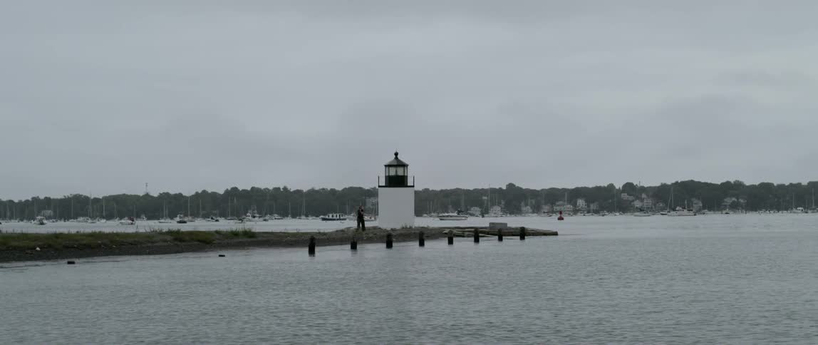 A person is visible standing on a jetty near a lighthouse in a coastal area