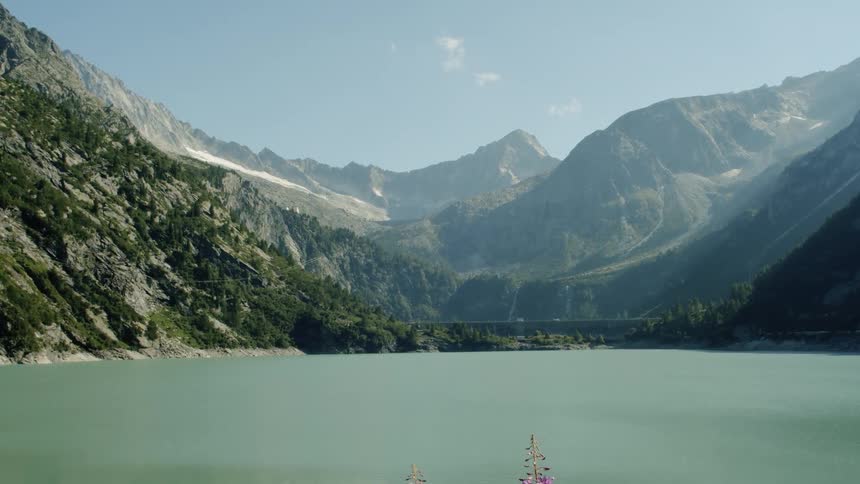 A massive lake sits in a recess within a towering and rocky mountain range under a clear blue sky