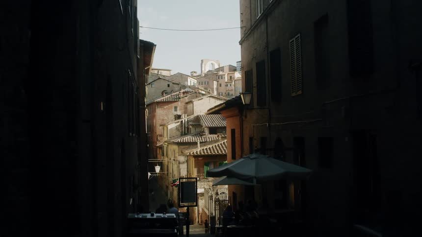 From within a darkened alleyway a neighborhood can be seen that is densely filled with older residential buildings