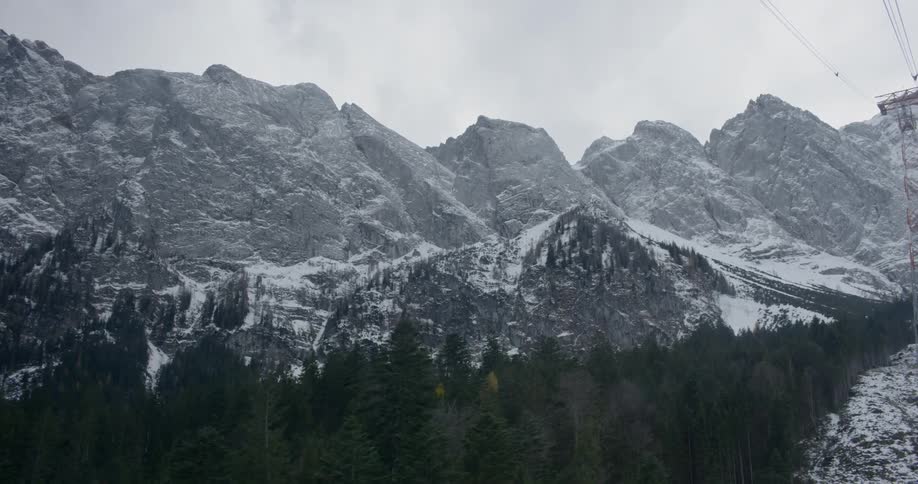 An aerial view of trees in snowy mountains on a cloudy day