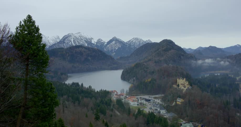 A castle in a small village surrounded by trees and snow capped mountains
