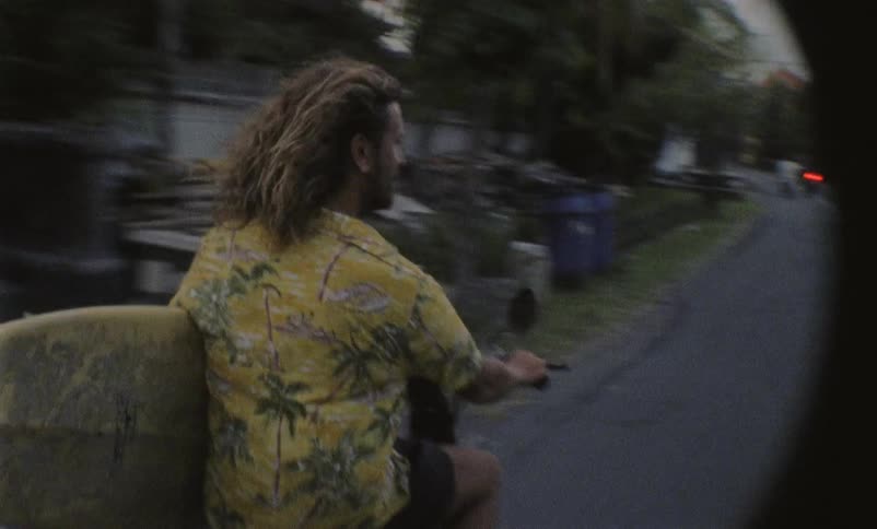 Man with surfboard riding a motorcycle
