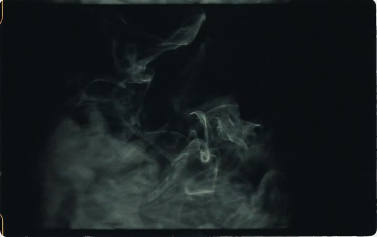 Camera taking photo of smoke being blown against a black backdrop