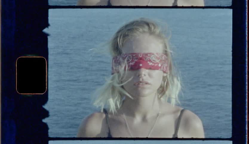Blonde blindfolded girl stands in front of the sea during daylight