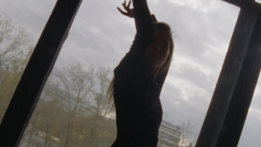 A female model holds a bottle of perfume and stretches her arms above her head