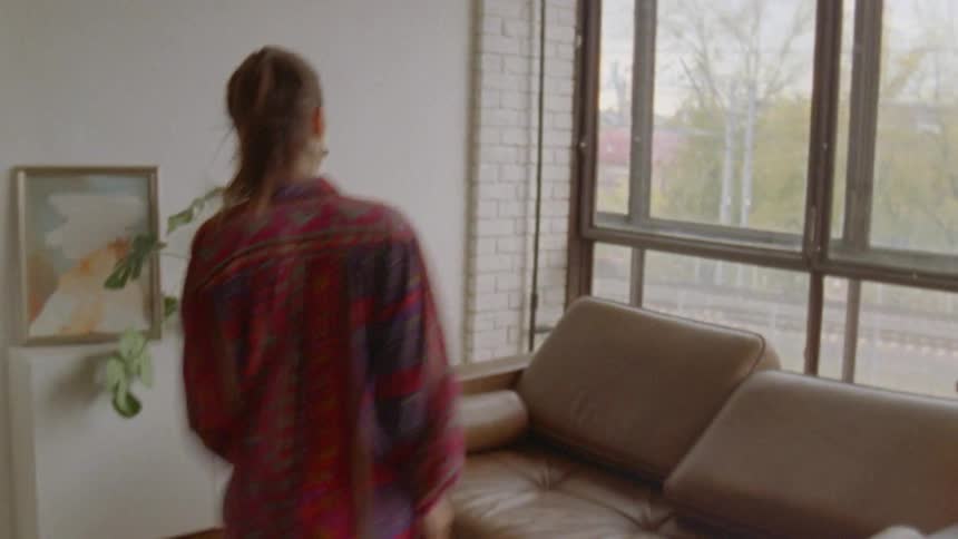 A woman jumps to lay on a brown leather couch near a window