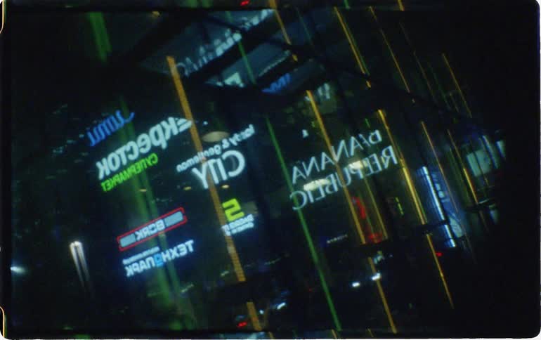 The reflections from several illuminated signs can be seen on a glass surface at night