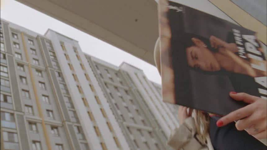 A young woman stands on a street corner holding an album