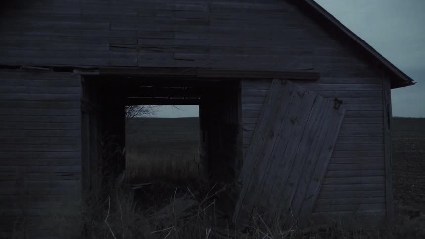 Panning into the interior of a dilapidated shack in front of a barren tree and then out to a dirt field