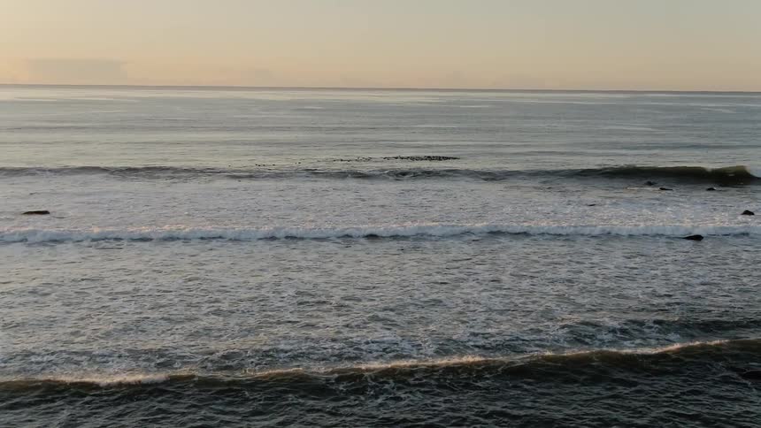 Waves crash in an ocean while the sun sets
