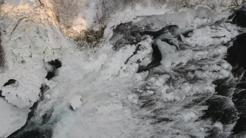Water falls down a snow and ice covered cliff
