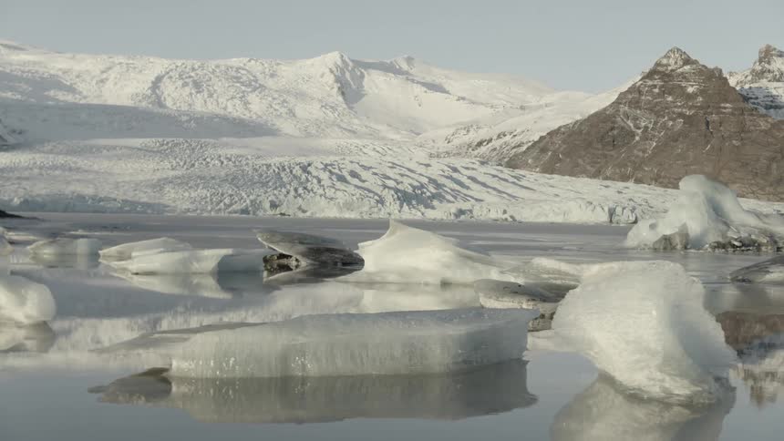 Sea ice near snow covered slopes and mountains under a clear blue sky