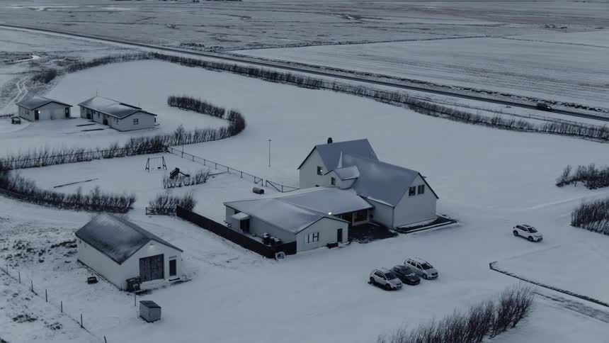Cars drive past farm buildings surrounded by snow