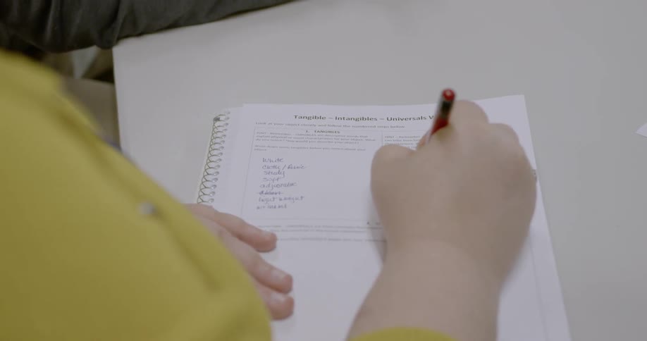 A woman is writing lists of words with a pen into columns located on a vocabulary worksheet