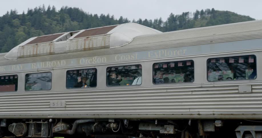 A passenger train moves slowly along the track beside a mountain