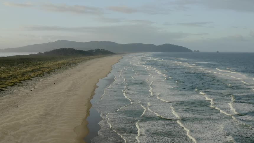 Ocean waves crashing onto a flat sandy beach with hills in the distance