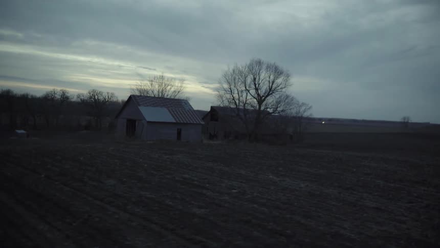 A cloudy sky over a shed and barn in a field