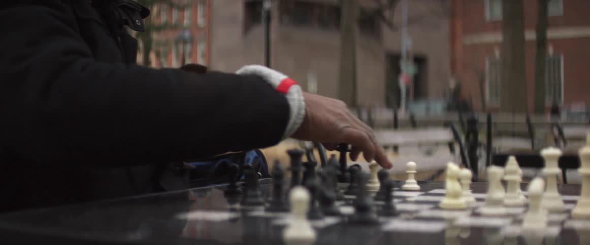 A man sitting at an outdoor chess table makes a move