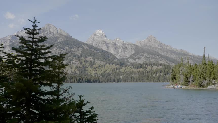 A river flows through a forested area at the foot of a mountain range