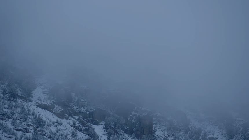 Thick fog descending on a rocky snow covered mountain slope