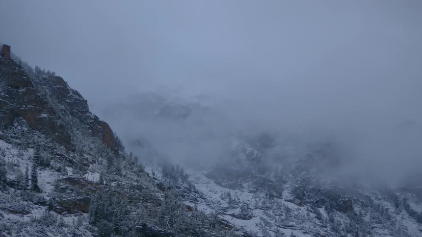 A thick layer of clouds and fog envelope a snow covered mountain range in winter