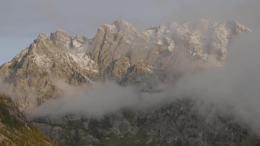 Clouds hang around snow dusted rocky peaks and ridge