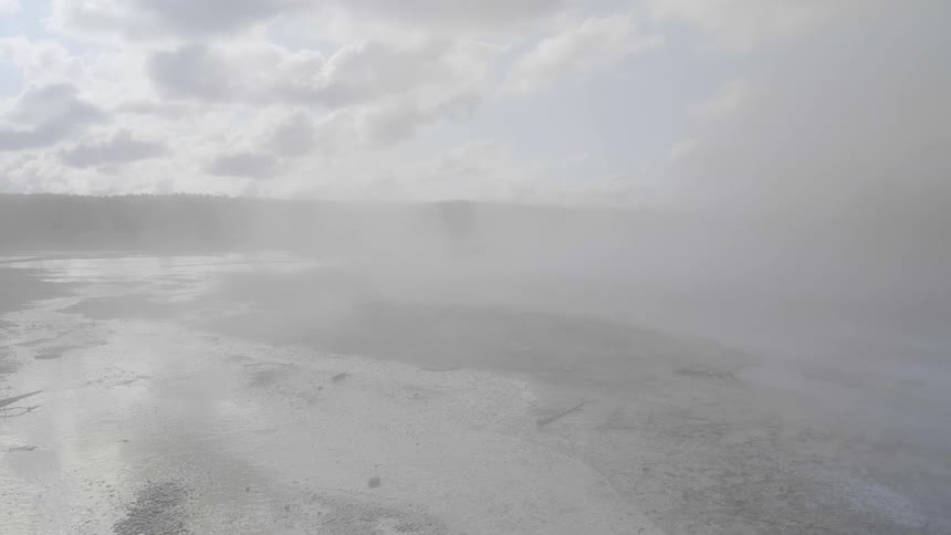 Steam from a hot spring billows over snow dusted landscape