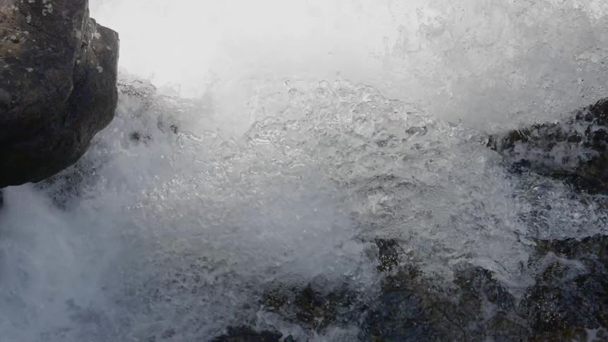 Rushing water is splashing violently over a group of rocks as it flows up and over the rocks and crashes down below
