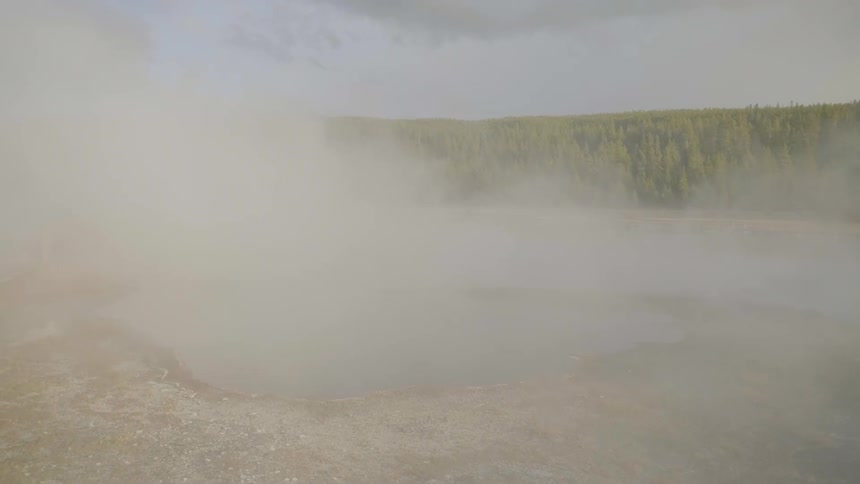 Steam rises off a hot spring and blows over the surrounding area