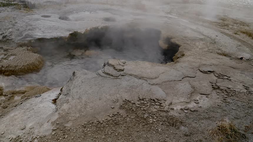 A puddle of boiling hot spring water with steam coming off of it