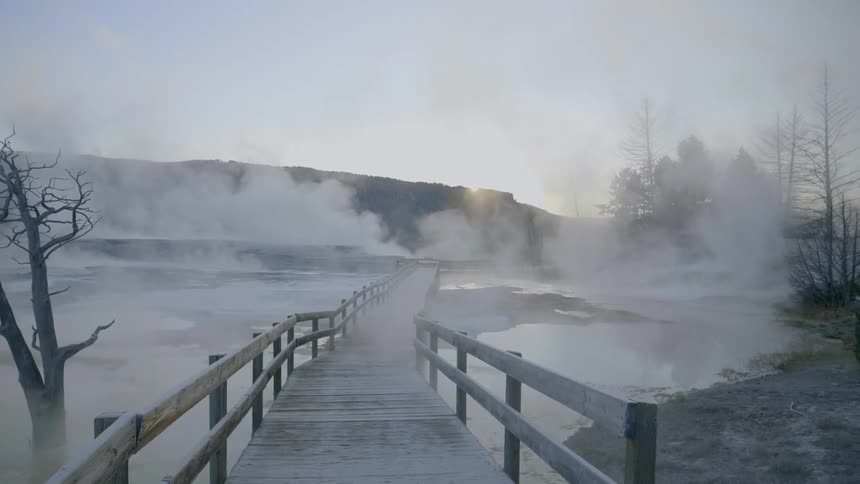 Steam pours up from the lake and covers a pedestrian bridge