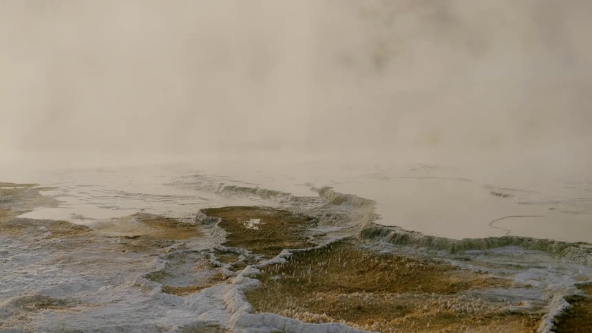 A huge cloud of steam hangs above the waters in a natural hot spring that is surrounded by large deposits of minerals