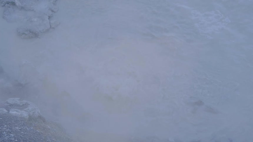 Steam rises from a bubbling hot spring on a winter day