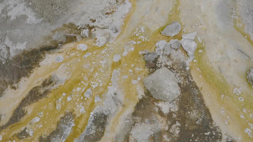 A snow dusted terrain with rocks and streams of yellow tinged mud