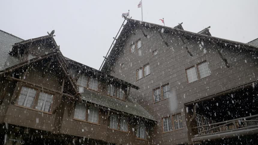 Snow falls on a large brown building with flags on its roof