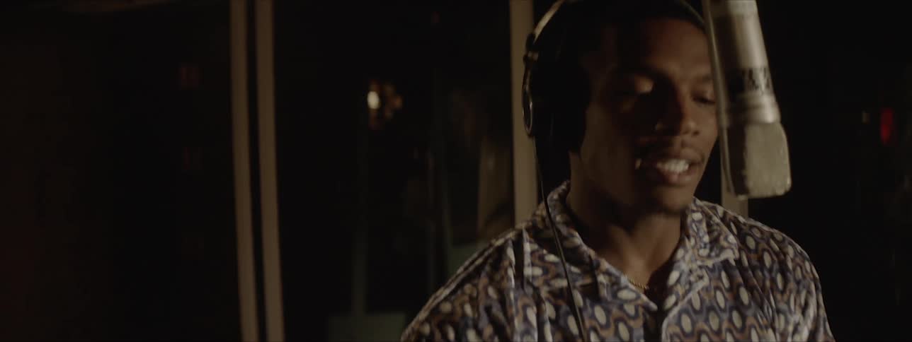 A young man recording a vocal track into a condenser microphone in a studio