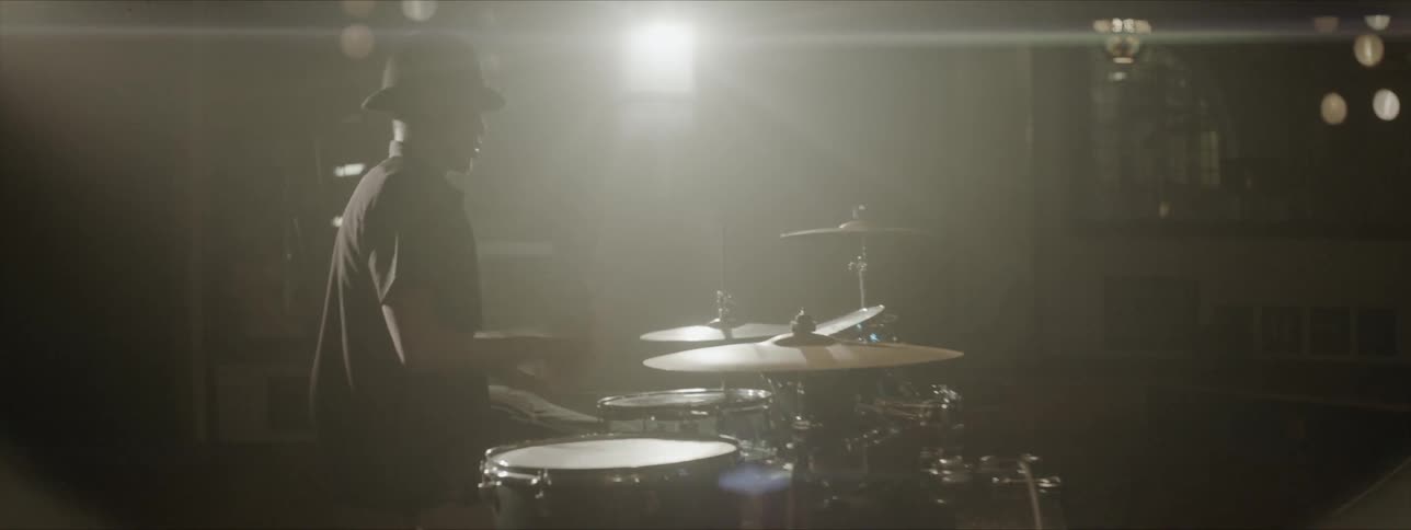 A black man in a hat playing the drums indoors