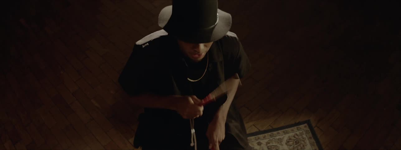 A man in a hat sits in front of a drum set as he plays the drums while repeatedly striking one of the cymbals
