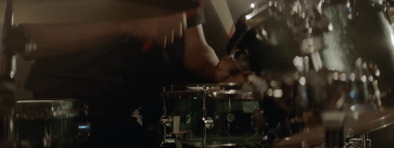 A man wearing a necklace and collared shirt is drumming