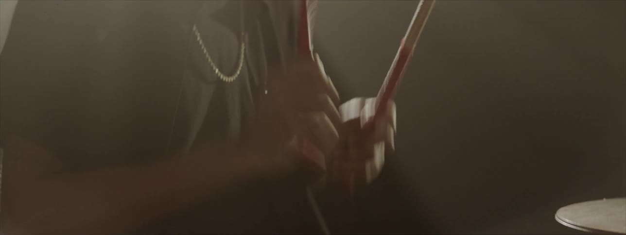 A seated male banging on drums using drumsticks