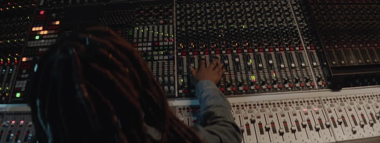 A black woman with dreadlocks is moving sliders on a music soundboard to make adjustments