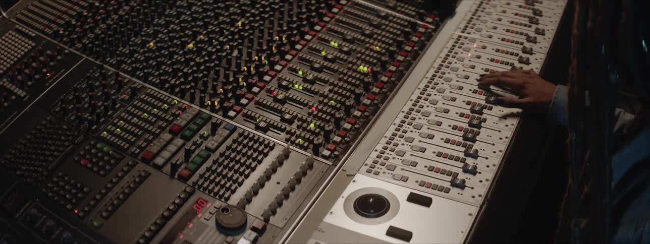 A person with dreadlocks sits at a mixing console and edits the settings