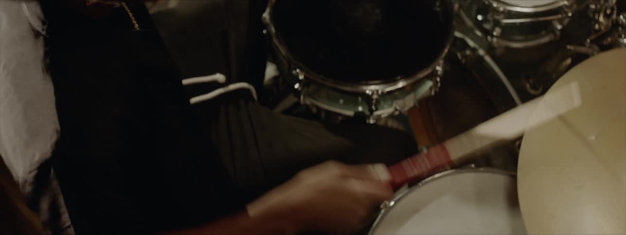 Black drummer wearing black hat plays drums at the stage