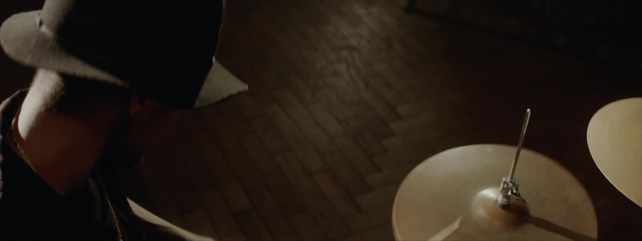 Black drummer wearing black hat plays drums at the stage