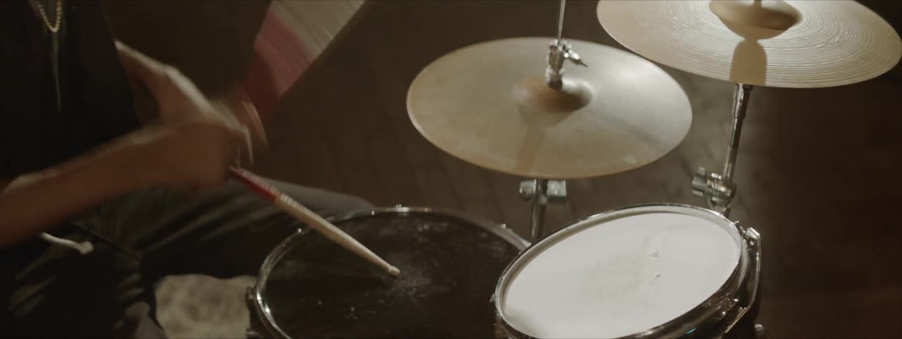 A man wearing a necklace collared shirt is drumming
