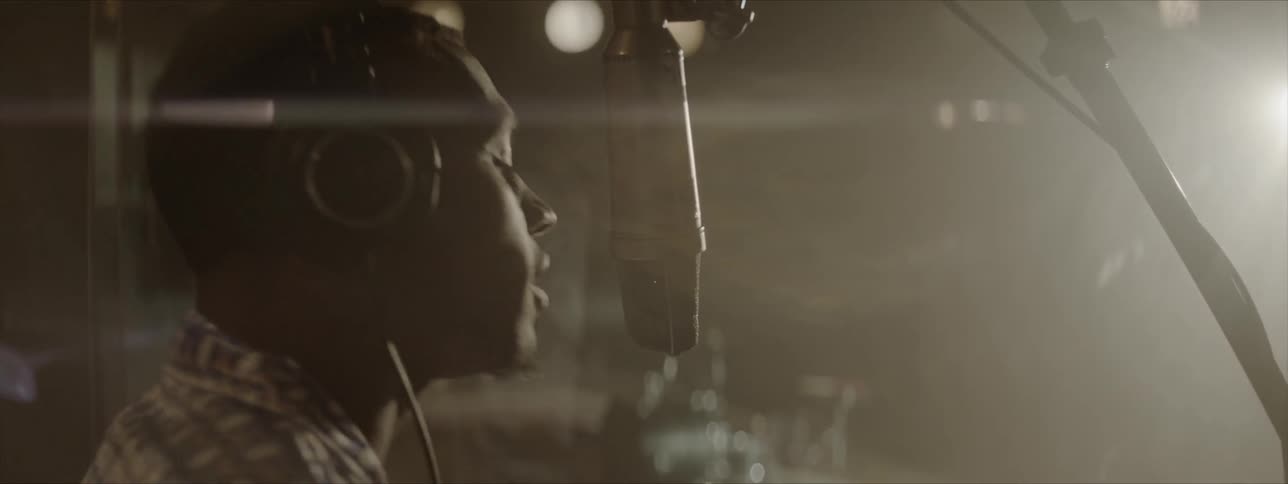 A young man recording a vocal track into a condenser microphone in a studio
