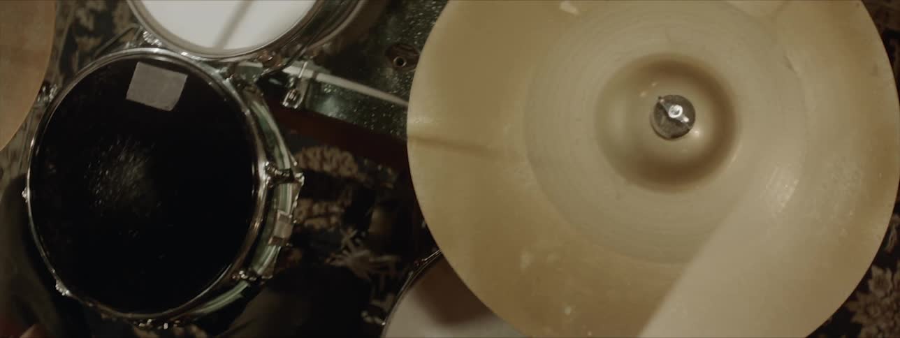 A man wearing a necklace and collared shirt is drumming
