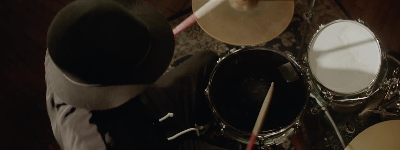A man in a hat and collared shirt is drumming open handed